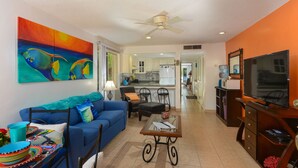 A living room with a sofa, coffee table, and chairs, a kitchen in the background, and a TV on the right. - Restful Oceanfront 1BR, Northshore,  Low Density building with only 12 condos. (Cozumel)