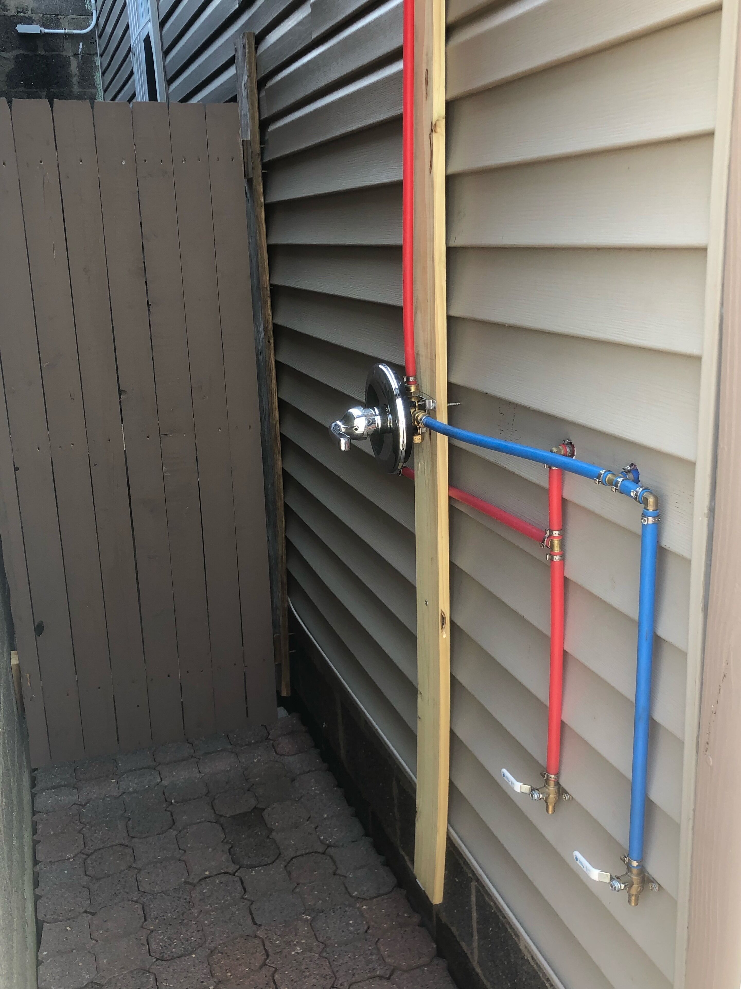 A utility area with a metal gate, a red and blue pipe system, and a wooden post.
