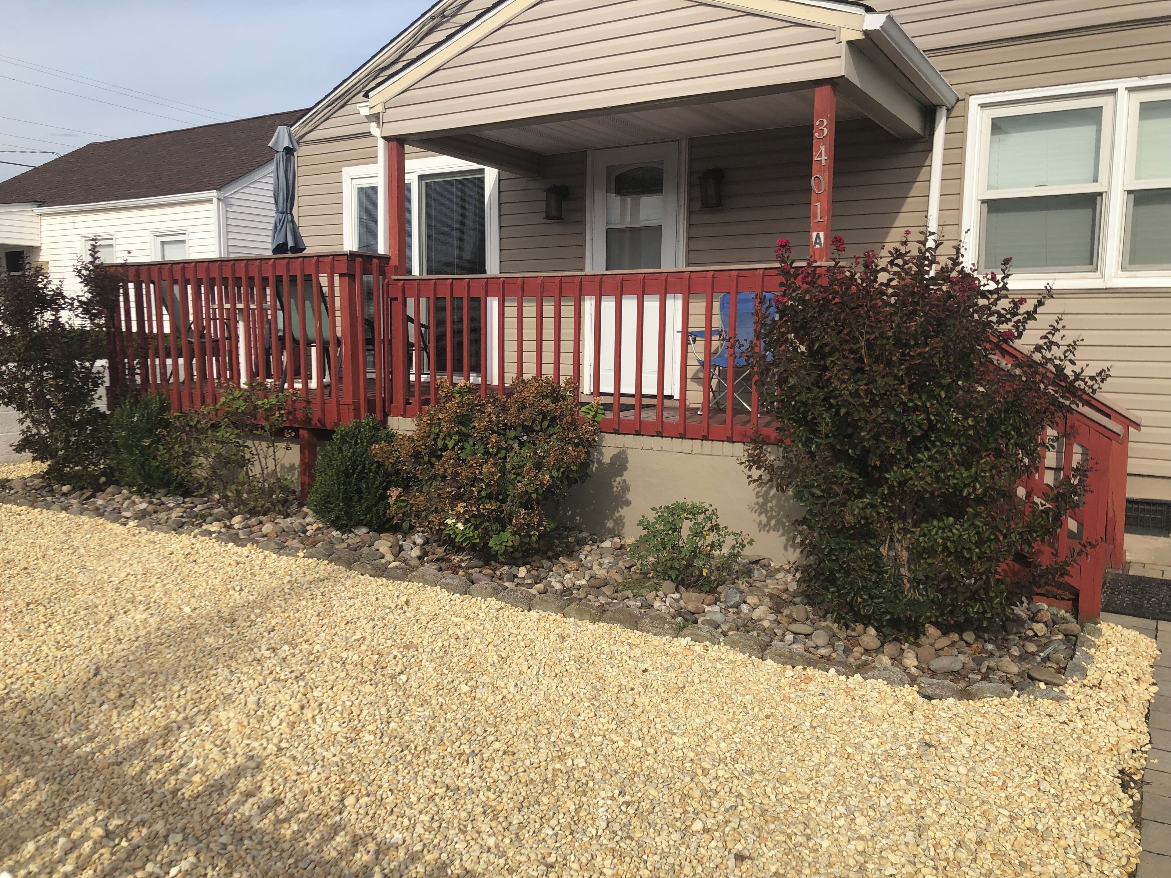 A residential house with a porch, a red railing, and a gravel driveway.