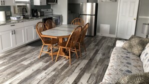 A compact kitchen with white cabinets, a stainless steel refrigerator, and a dining table with wooden chairs. - GORGEOUS BEACH HOUSE, TOP LOCATION! WALK TO BEACH, ICE CREAM, EATERIES. DOGS OK (Brigantine)