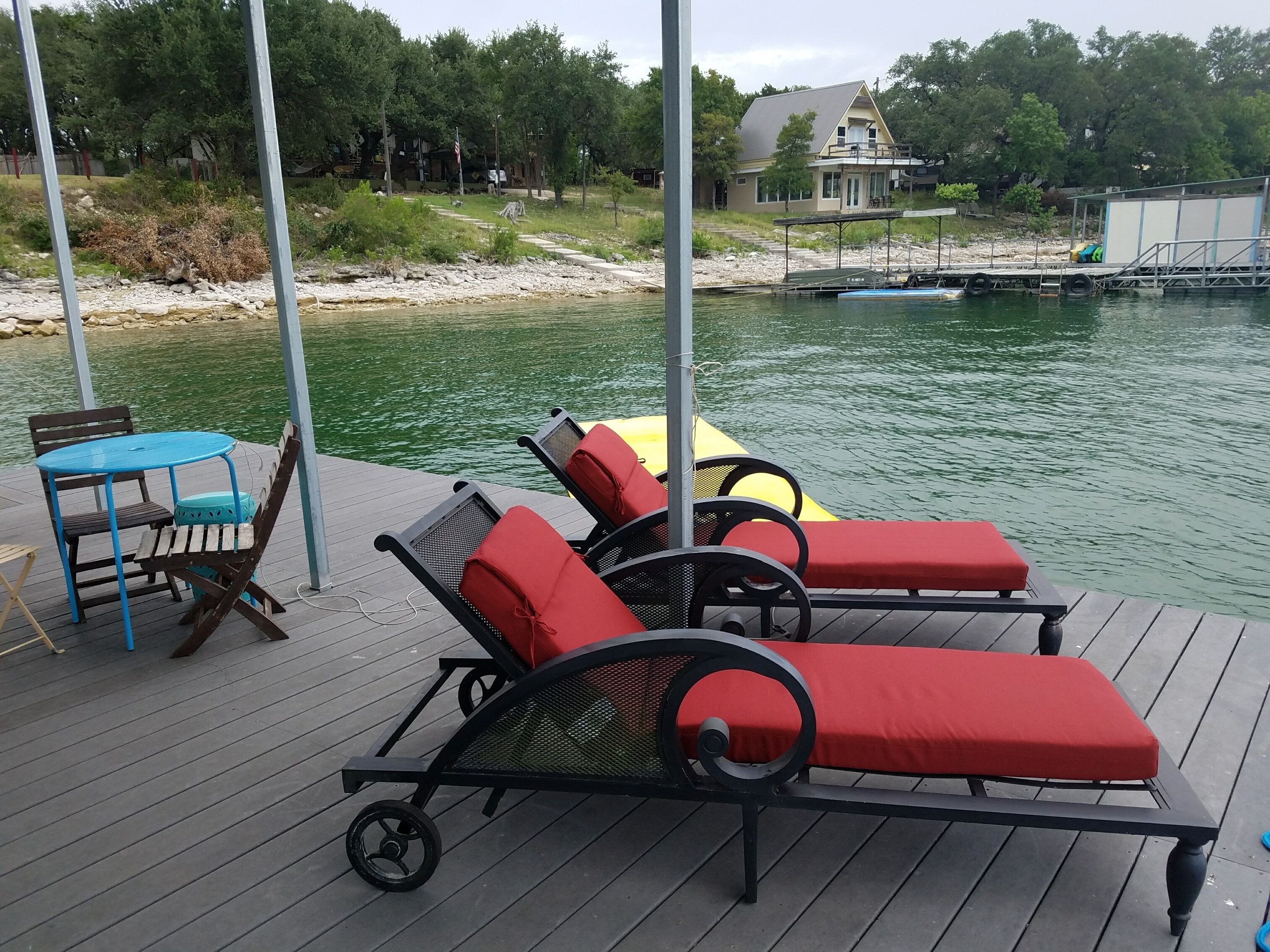 A deck with lounge chairs and a table, overlooking a body of water with a house in the background.