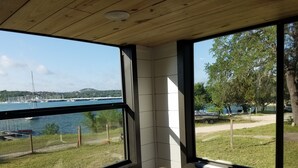 A room with large windows offering a view of a marina with boats and a grassy area with trees.