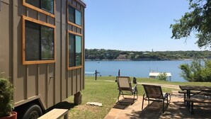 A small cabin with a view of a lake, outdoor seating, and a picnic table.
