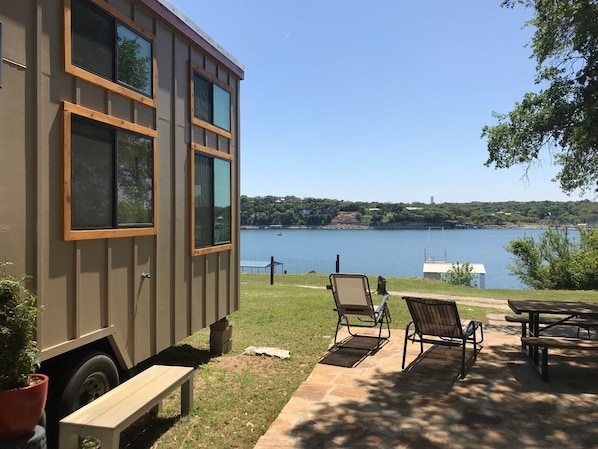 A small cabin with a view of a lake, outdoor seating, and a picnic table.