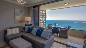 A modern living room with a sofa, ottoman, and a table with chairs, overlooking a scenic ocean view.
