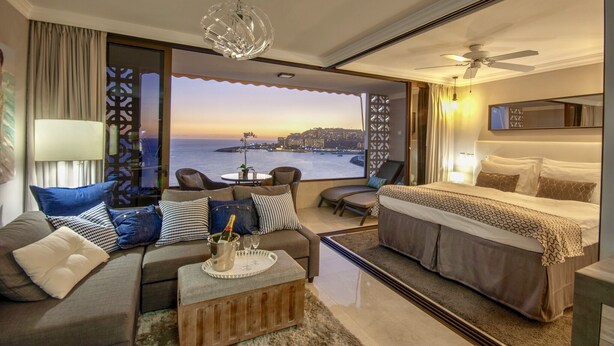 A modern hotel room with a balcony, a bed, a sofa, and a coffee table.