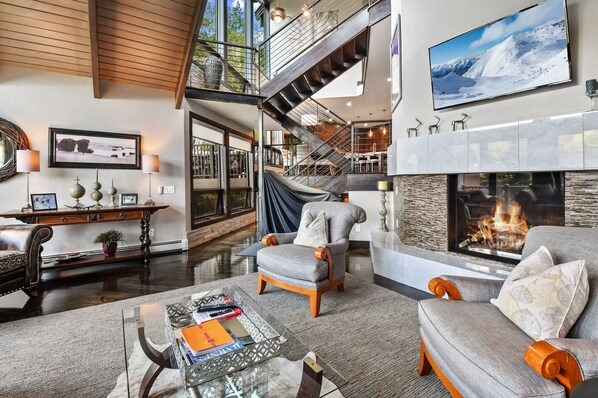 A spacious living room with a fireplace, a staircase, and a large TV on the wall.