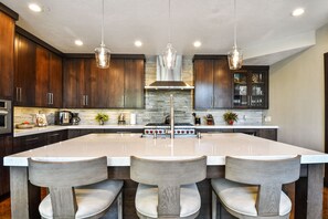 A modern kitchen with dark wooden cabinets, a large island with bar stools, stainless steel appliances, and pendant lighting.