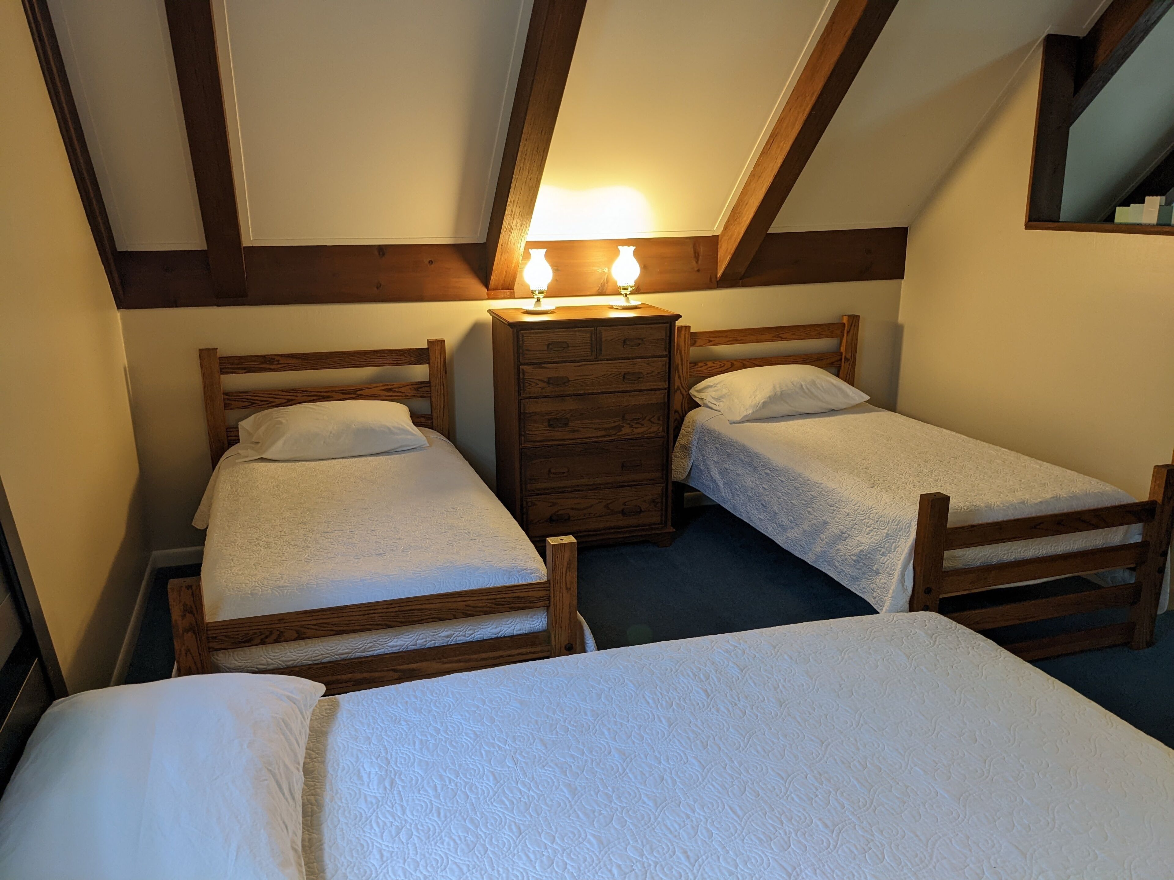A room with two wooden beds, a wooden dresser, and a small table with two lamps.