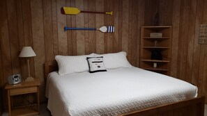 Ein Zimmer mit Holzwänden, einem Bett, einem Nachttisch mit Lampe und einem Regal mit einem Schild.