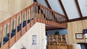 Una escala de fusta amb barana que condueix a un nivell superior. Hi ha un armari de fusta amb portes de vidre que conté diferents objectes.