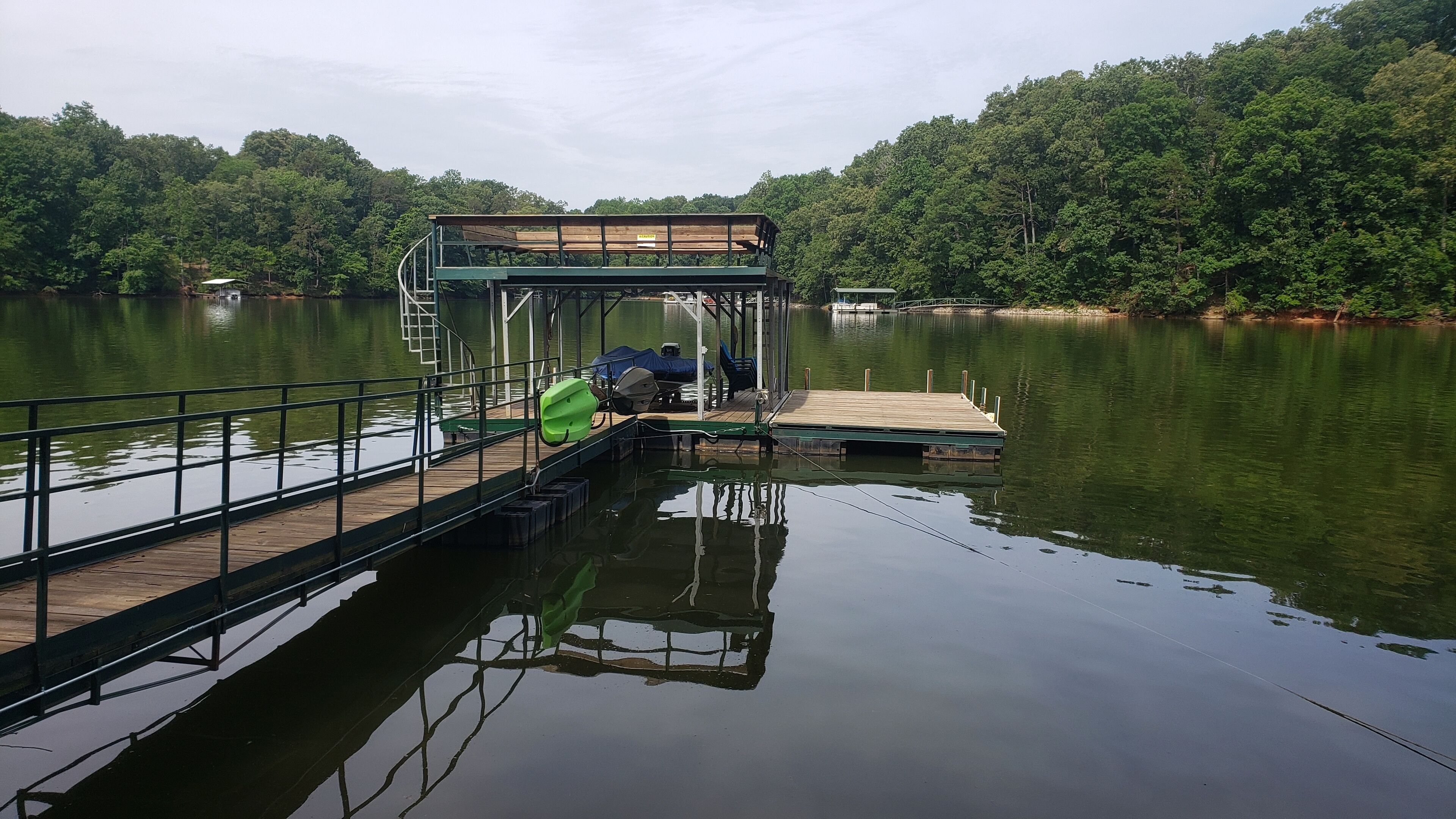 Eine Anlegestelle, die in einen ruhigen See führt, mit überdachter Sitzgelegenheit und einem kleinen Boot.