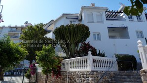 A white building with balconies, a stone wall, and a cactus.