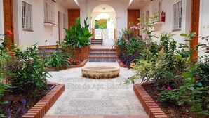 A courtyard with a central fountain, surrounded by brick walls and potted plants.