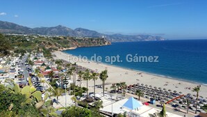 A coastal town with a beach, palm trees, and mountains in the background.