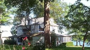 A large, two-story house with a stone facade, surrounded by lush greenery and a lake view.