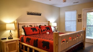 Una cama de madera con colcha temática de osos, en rojo y negro, dos lámparas de noche y un mueble pequeño.