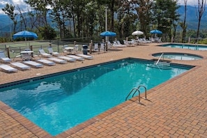 A pool area with lounge chairs and umbrellas, surrounded by trees and mountains.