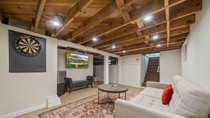 A cozy living room with a dartboard, a television, and a staircase leading to an upper level. - Historic Craftsman Bungalow, Just Steps to Downtown ~HOT TUB!~ (Bend)