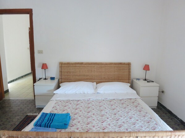 A bedroom with a bed, two nightstands, two lamps, a blue towel, and a patterned bedspread.