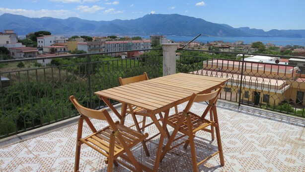 A terrace with a wooden table and chairs, overlooking a coastal town with mountains in the background. - Pompei, Vesuvio and Naples bay view (Trecase)