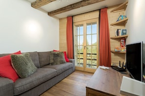 A living room with a grey sofa, red and grey cushions, a wooden coffee table, a TV, and a bookshelf with books and games. - Chalet Grand Roi - La Tzoumaz, 4 Vallees (La Tzoumaz)