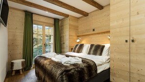 A wooden-paneled bedroom with a bed, a small stool, and a window with curtains. - Chalet Grand Roi - La Tzoumaz, 4 Vallees (La Tzoumaz)