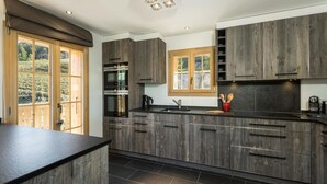 A modern kitchen with dark wood cabinets, a black countertop, and a large window providing natural light. - Chalet Grand Roi - La Tzoumaz, 4 Vallees (La Tzoumaz)