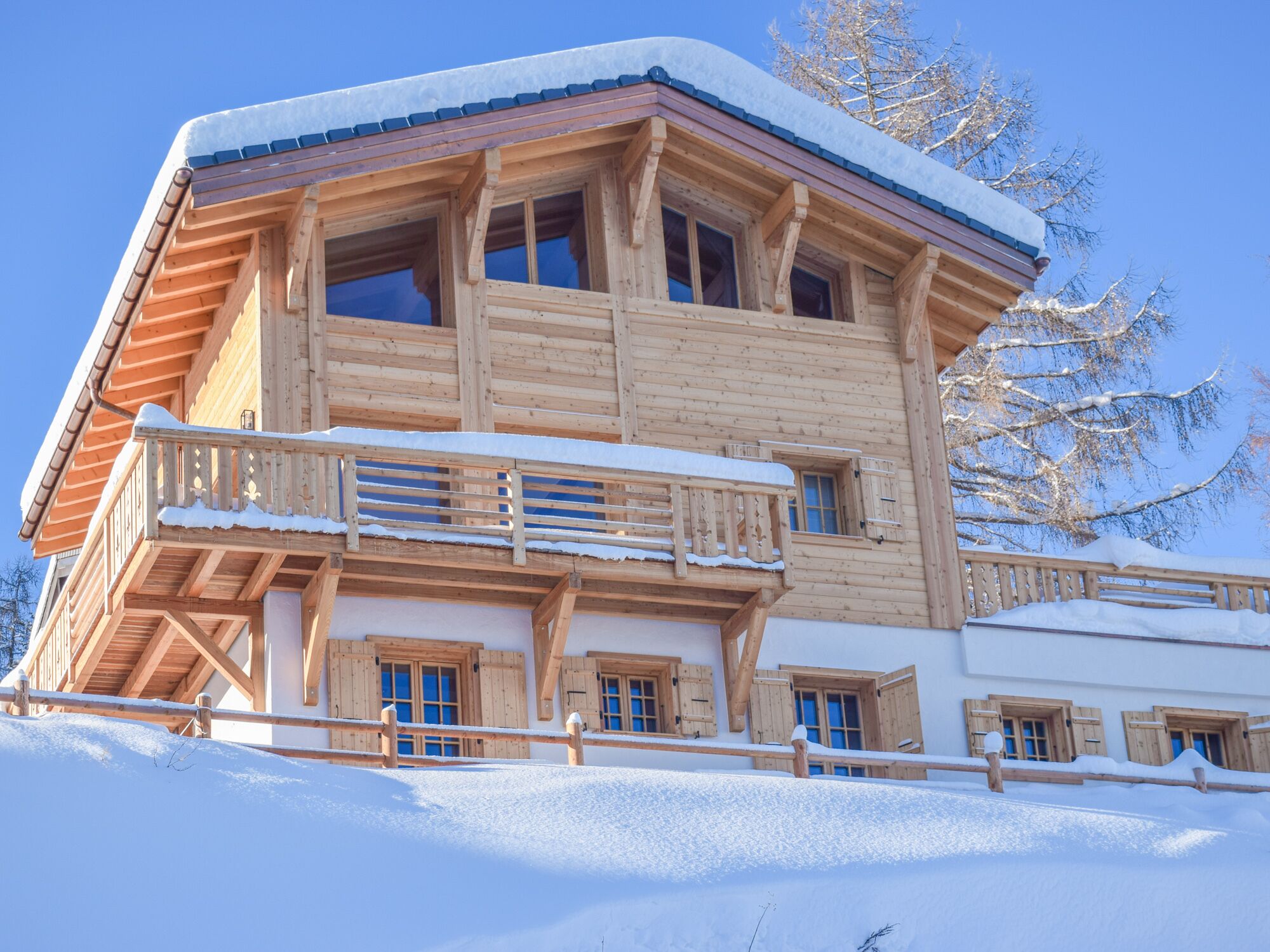 Un chalet de madera con balcón, múltiples ventanas y un techo cubierto de nieve.