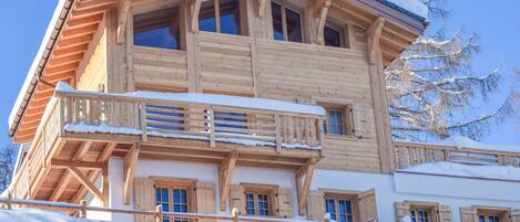 Un chalet de madera con balcón, múltiples ventanas y un techo cubierto de nieve.