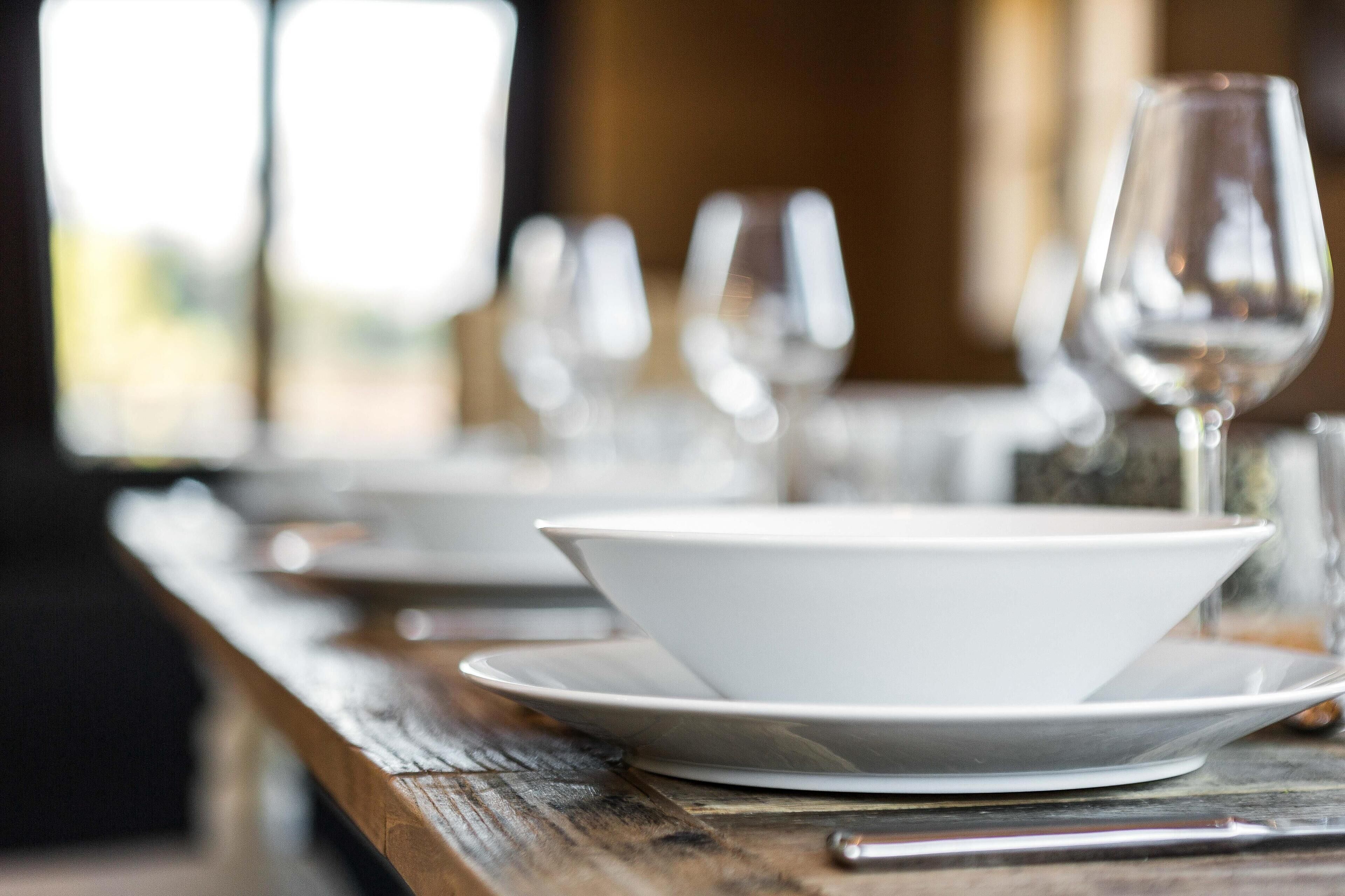 A dining table with white plates and wine glasses, set in a rustic wooden table setting.