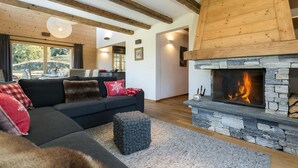 A cozy living room with a stone fireplace, a dark sofa with red and white cushions, and a wooden ceiling. - Chalet Grand Roi - La Tzoumaz, 4 Vallees (La Tzoumaz)