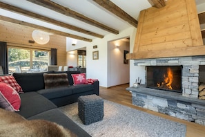 En hyggelig stue med en stenvægspejs, en mørk sofa med røde og hvide puder, og et træloft.
