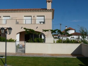 A two-story building with a beige facade, a tiled roof, and a small balcony.