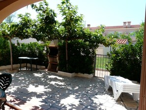 An outdoor patio with a stone floor, a table, a grill, and a white folding chair.
