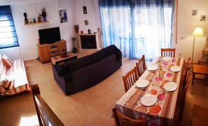 A living room with a sofa, TV, and fireplace. Dining area with table set for four.