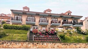 A multi-story hotel with balconies, a stone retaining wall, and a landscaped area with flowers. - Casa de Las Flores Apartment with private garden in front of the beach of Comillas (Comillas)