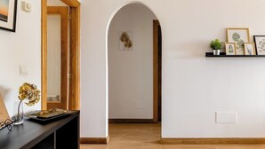 A hallway with a wooden door, a black console table with a vase and a picture frame, and a wall with framed botanical prints. - Casa de Las Flores Apartment with private garden in front of the beach of Comillas (Comillas)