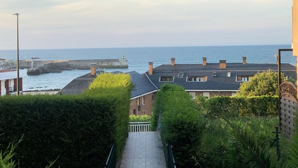 A coastal residential area with a paved pathway leading to a sea wall and a lighthouse in the distance. - Casa de Las Flores Apartment with private garden in front of the beach of Comillas (Comillas)