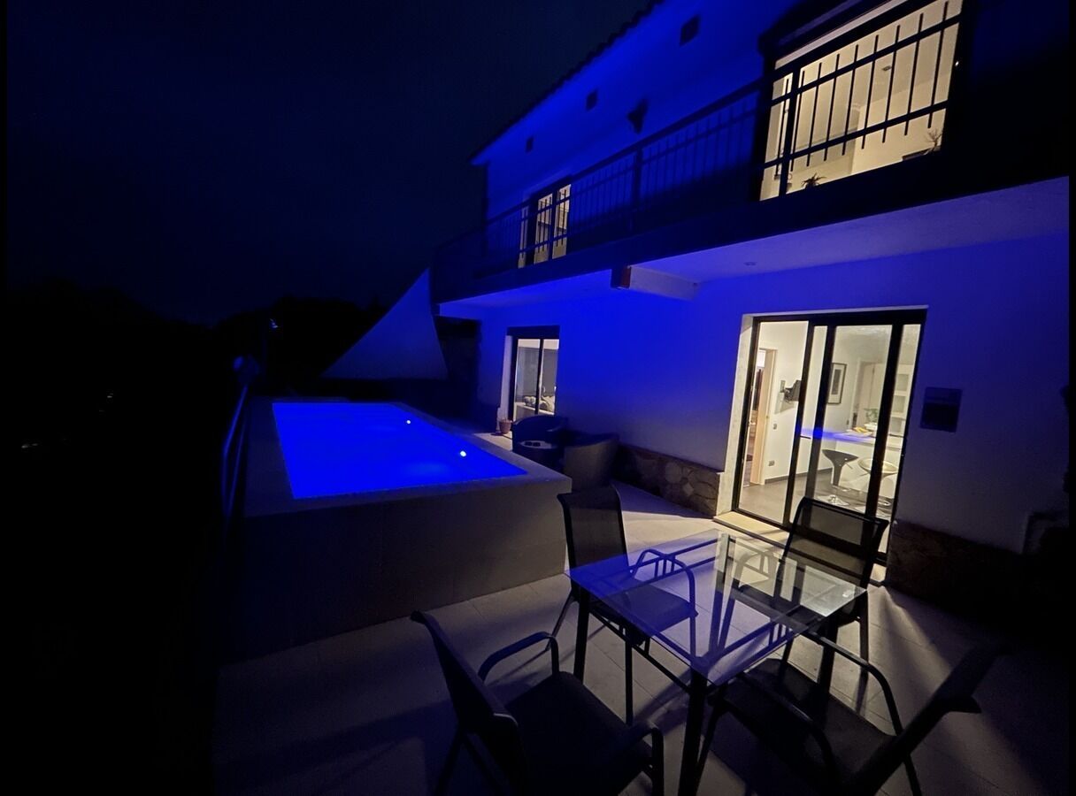 A pool area with a glass table and chairs, a balcony, and a building with windows.