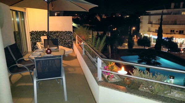 A balcony with a table set for dining, a pool, and a railing with plants.
