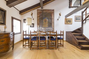 Un comedor con una mesa y sillas de madera, una araña y una escalera.