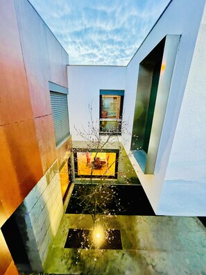Un edificio moderno con un patio estrecho, una ventana pequeña con persianas y un elemento acuático reflectante.