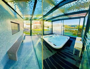 Een modern binnenzwembad met een jacuzzi, glazen wanden en uitzicht op een groen landschap.