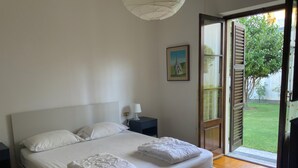 Quarto com cama, mesa de cabeceira, abajur, quadro e porta de correr para um jardim.