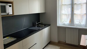 Uma cozinha moderna com armários brancos, bancada preta, micro-ondas embutido e uma janela com cortinas leves.