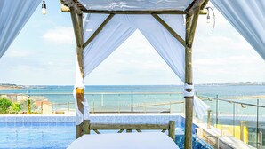 Ein hölzernes Bett mit weißem Baldachin mit Blick auf einen Swimmingpool und einen Strand.