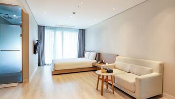 Una habitación de hotel moderna con una cama, un sofá, una mesita y un baño visible a través de una puerta abierta.