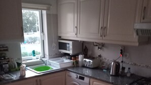 Une cuisine compacte avec des meubles blancs, un lave-linge, un four à micro-ondes, un grille-pain et un évier.