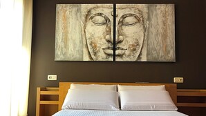 Ein Bett mit weißen Leinen und einer blauen, strukturierten Decke, ein hölzernes Kopfteil und ein großes abstraktes Gemälde an der Wand.